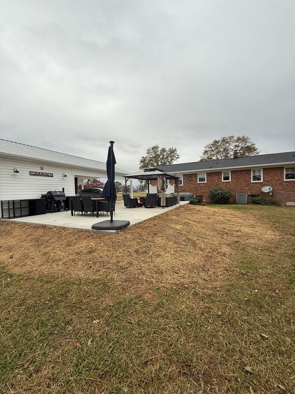 A patio with outdoor furniture and a large umbrella, situated between two houses with a lawn covered in wood chips.