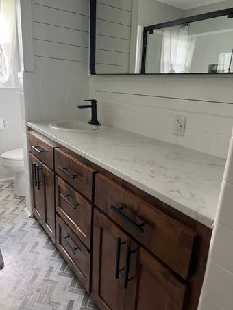 A modern bathroom vanity with dark wood cabinets, a white marble countertop, a black faucet, and white horizontal walls.
