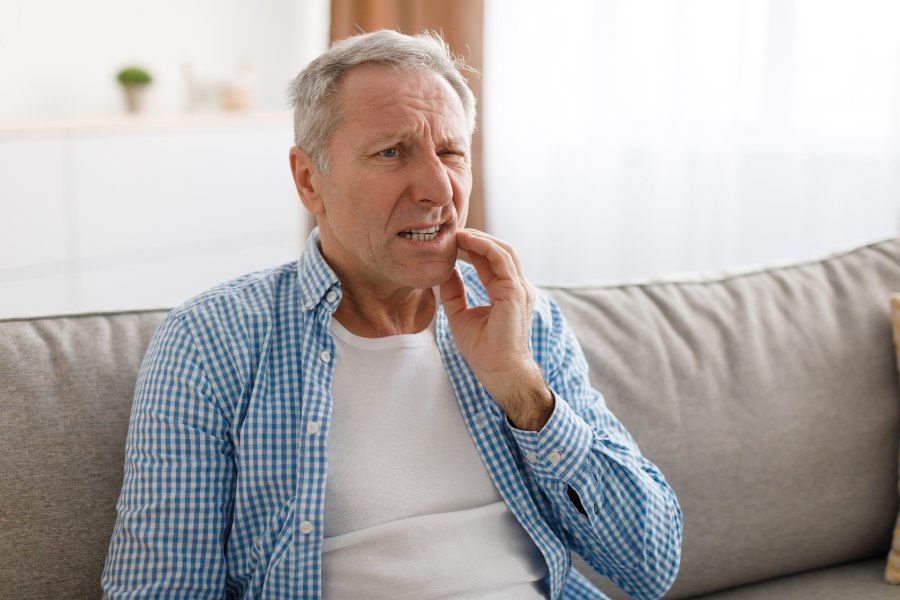Man sitting on a couch, holding his jaw, showing signs of tooth pain.