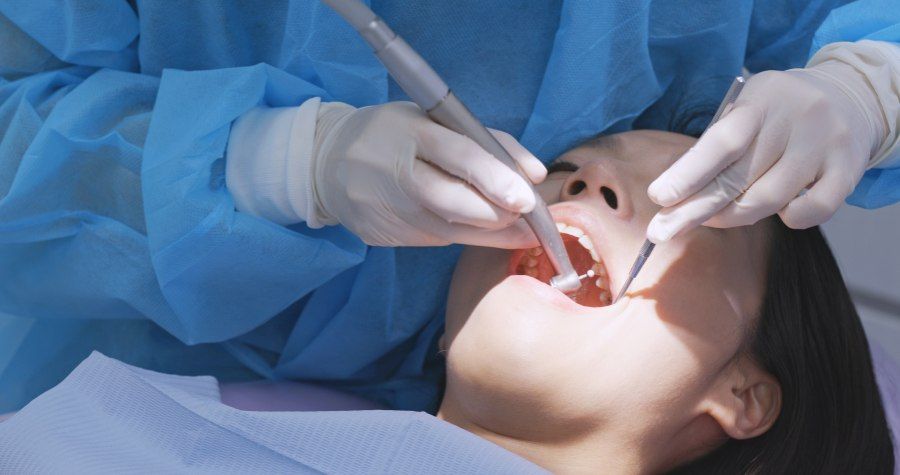 Dentist performing dental work on a patient in a medical setting.