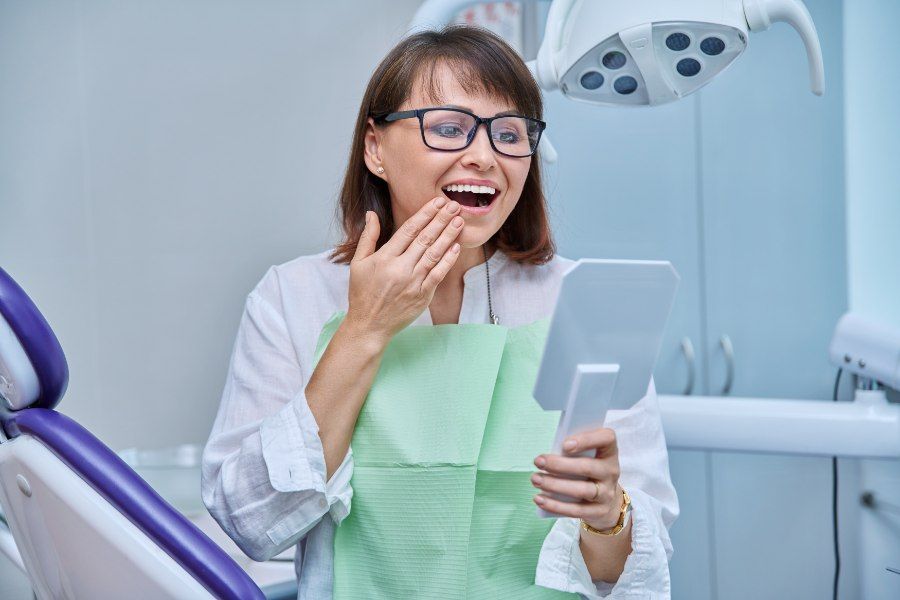 Woman in dental chair looking in a mirror, surprised expression, white teeth visible, dental office setting.