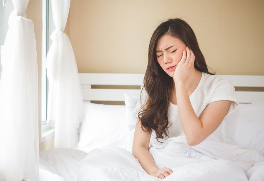 Woman in bed holding cheek, appearing to have a toothache.