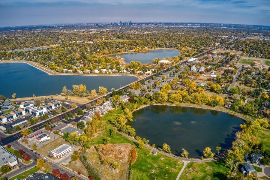 Aerial view of three lakes, green space, and homes, with Denver skyline in the distance.