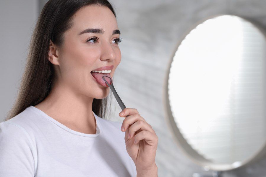 Woman scraping her tongue with a tongue scraper in front of a mirror, indoors.