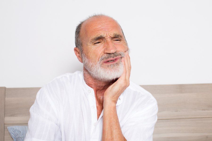 Man in white shirt holds jaw, grimacing, indicating tooth pain.