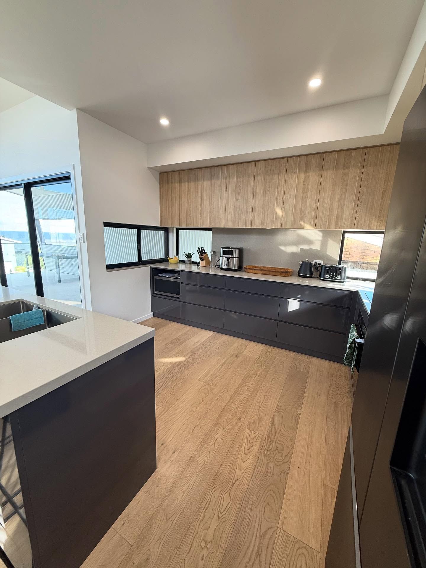 Modern kitchen with light wood floors, dark cabinets, and light wood upper cabinets — Barrington Coast Homes in Tallwoods, NSW