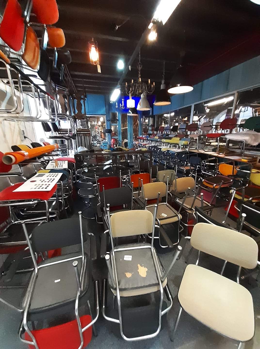 Een rommelig interieur van een meubelwinkel, gevuld met diverse stoelen in allerlei kleuren en stijlen.