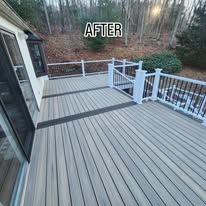 After view of a gray composite deck with white railing and wooded yard beyond.