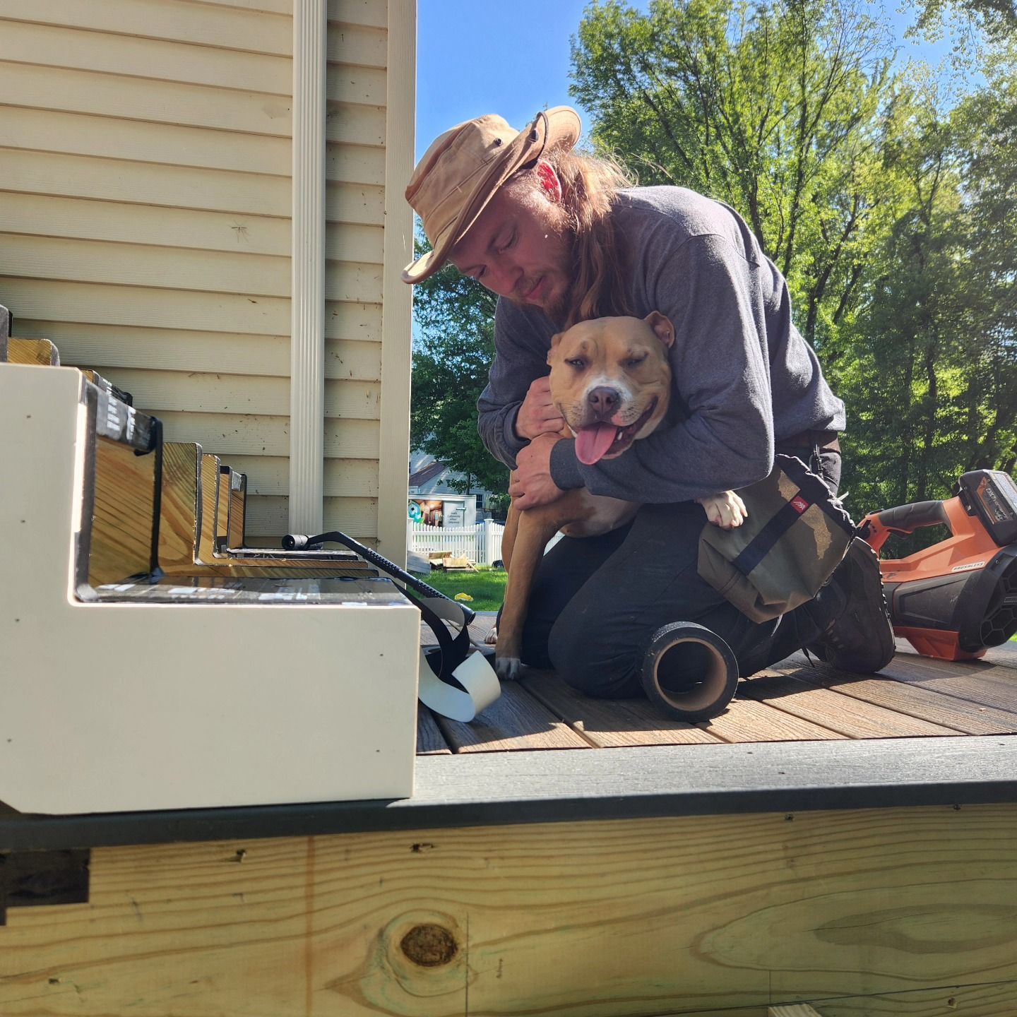Person kneels on a porch holding a happy dog beside a house, with tools and a generator nearby.