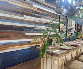 A rustic dining table with place settings and a large fern, set against a wall featuring horizontal wooden planks.