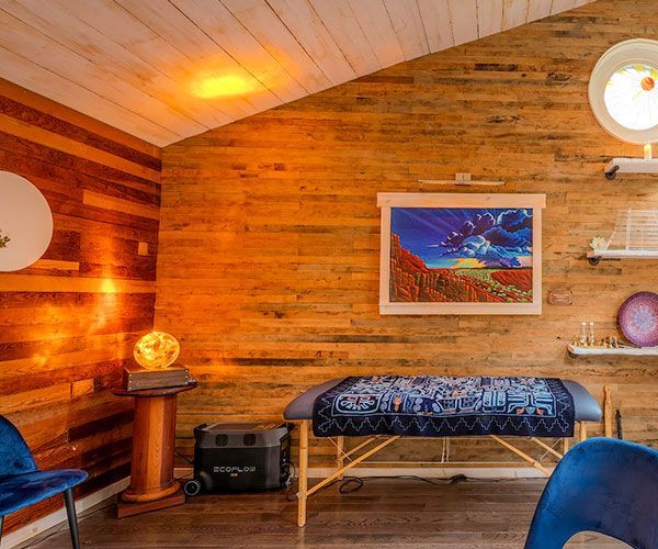 Cozy wood-paneled room with a bench, glowing lamp, framed artwork, and a blue chair