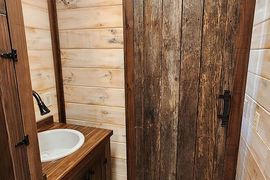 A bathroom vanity with a white sink and rustic wood walls next to a sliding barn door made of reclaimed wood.