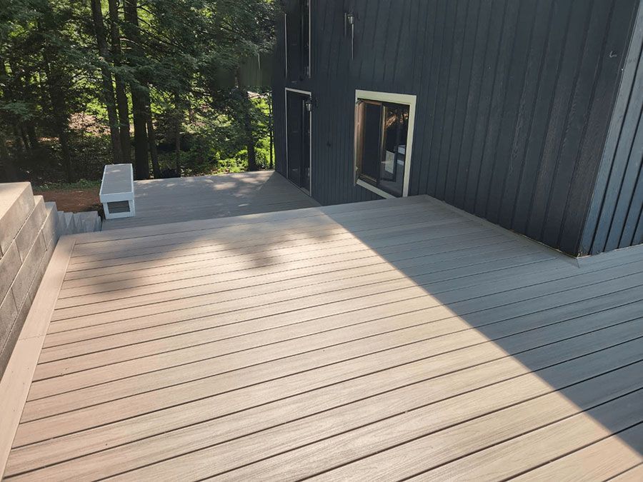 Wooden deck beside a dark house wall, with a white chair and trees in the background.