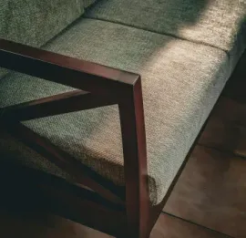 Close-up of a green upholstered couch with dark wooden armrest on a tiled floor