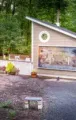 Outdoor memorial wall and garden in a wooded area, with a slanted-roof display and gravel path.