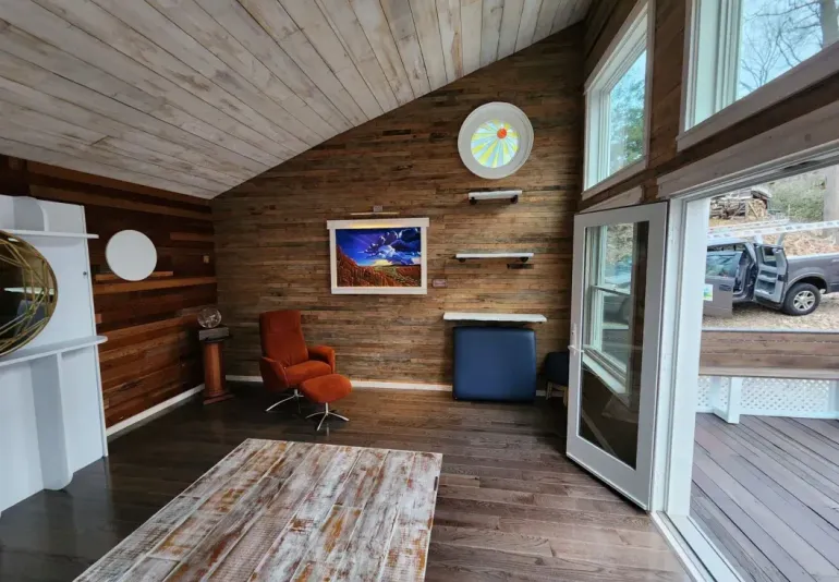 A luxury bathroom with a freestanding white tub, wood-paneled feature wall, marble floor, and floor-to-ceiling windows.