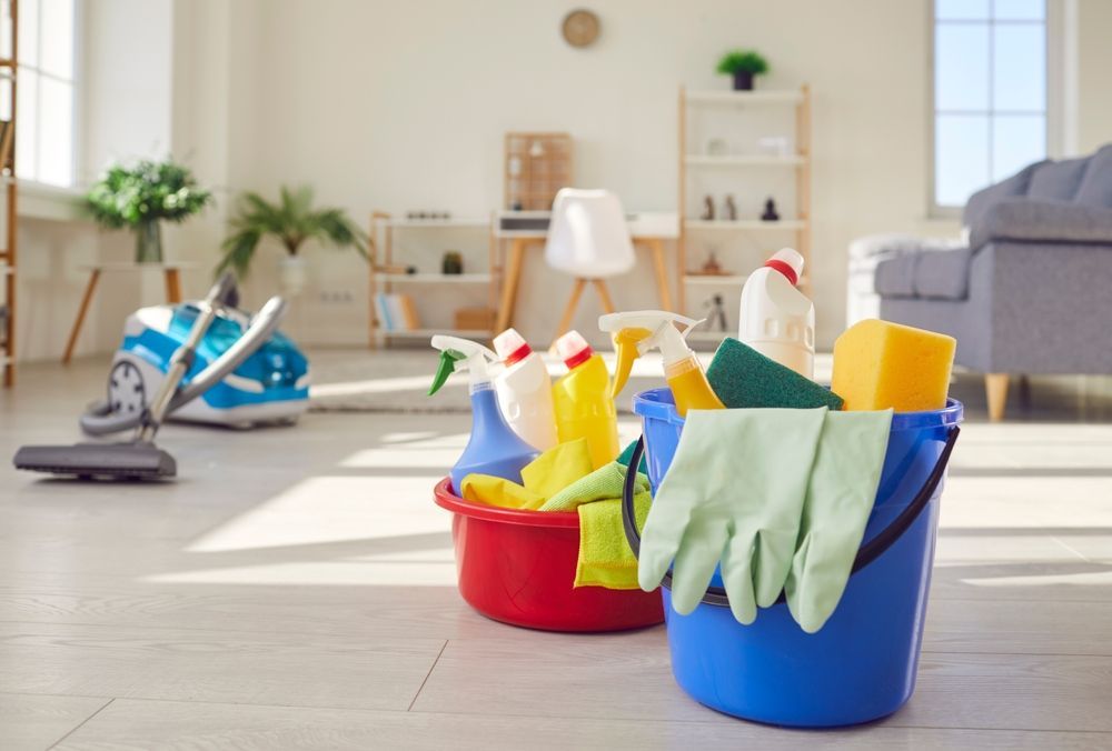 Cleaning supplies in red and blue buckets on a kitchen floor with a mop and gloves