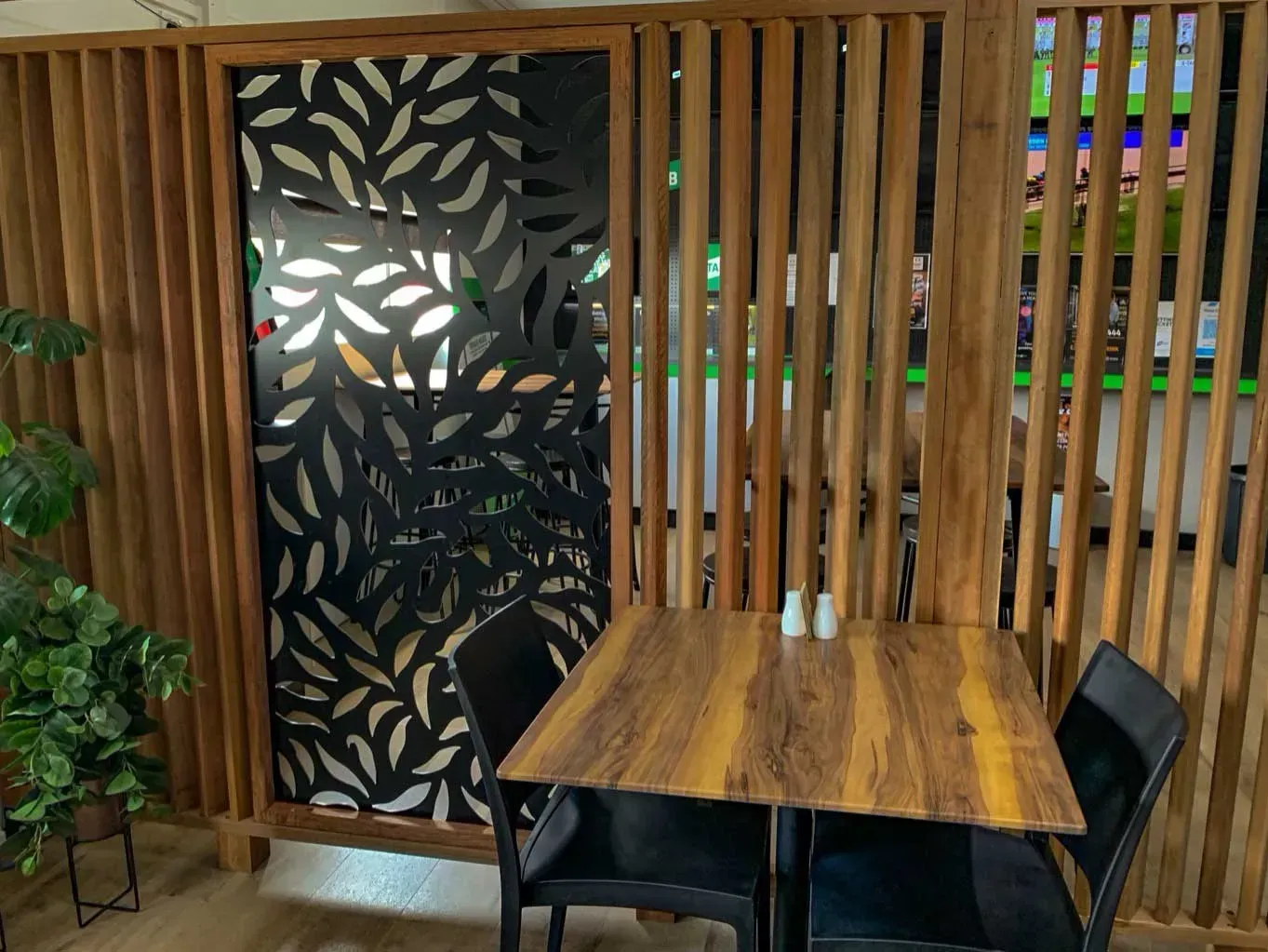 Restaurant booth with wooden slat dividers, black leaf-patterned screen, table, chairs — Boundary Creek Timber in Wallaville, QLD