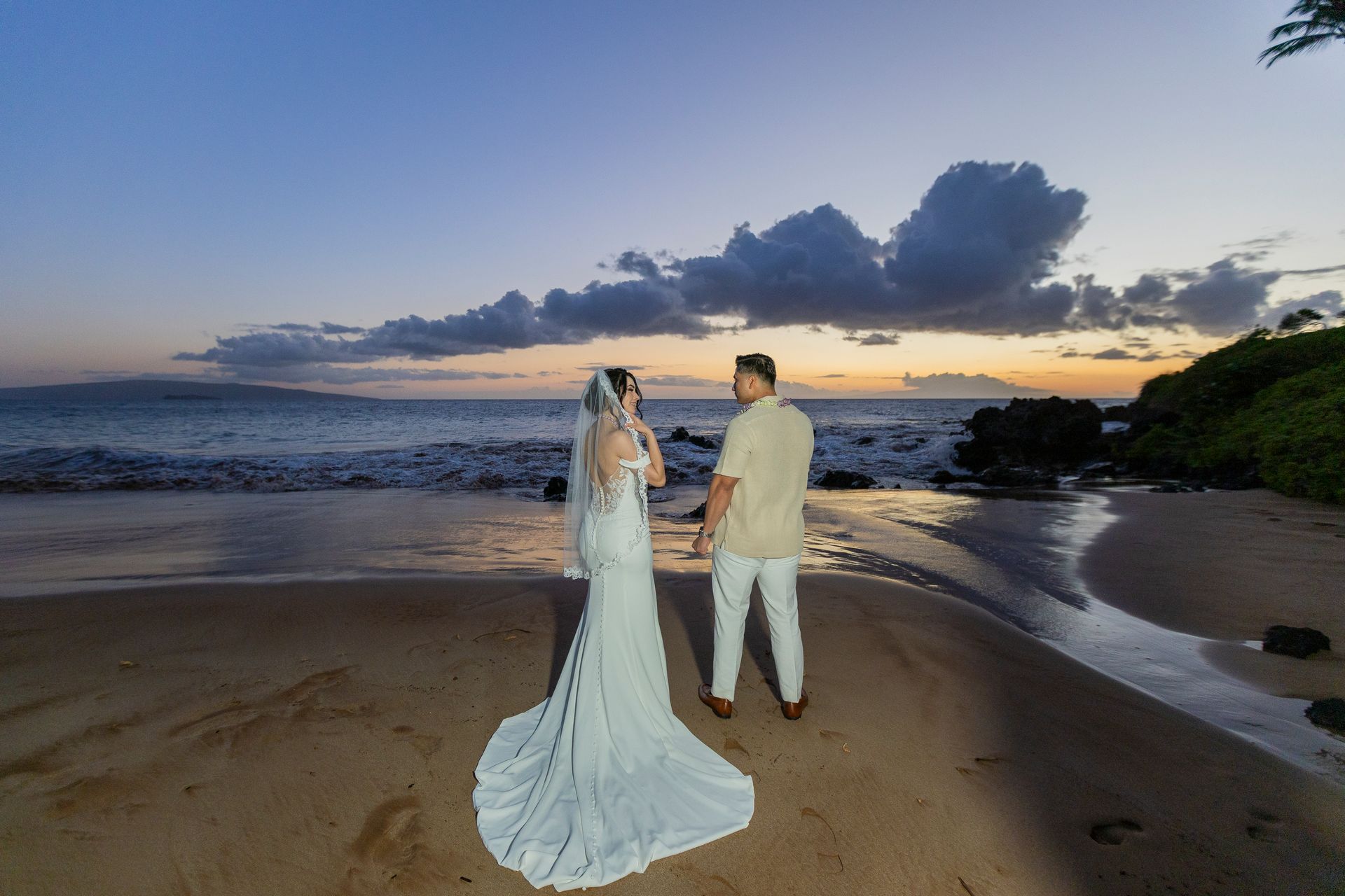 Bride and groom holding hands on a beach at sunset.