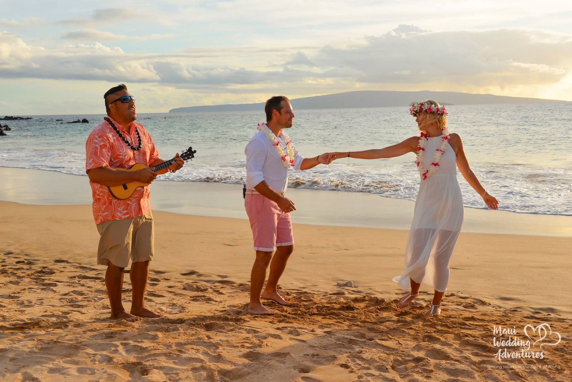 A man plays ukulele as a couple dances on a beach at sunset.