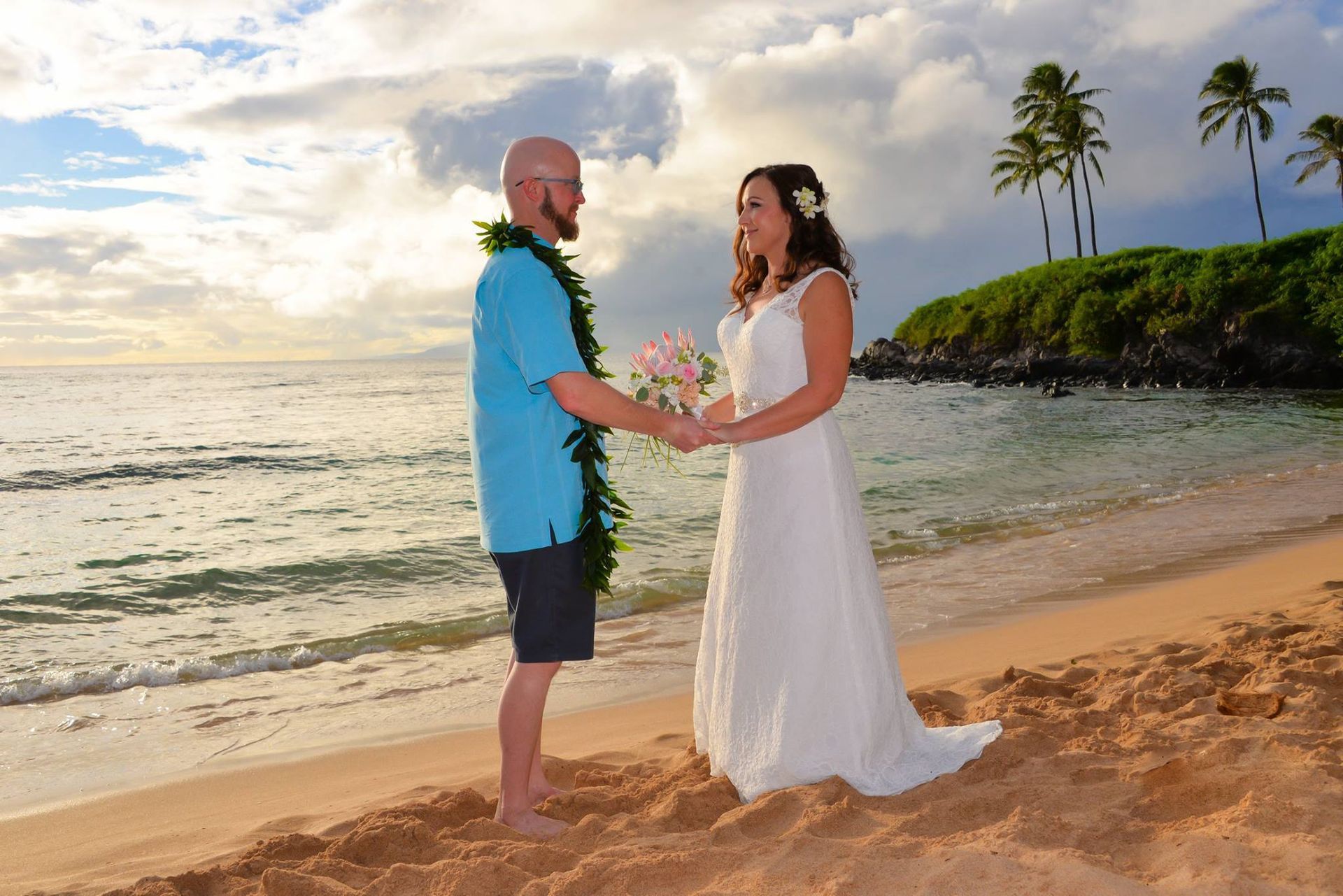 Couple holding hands on a beach, exchanging vows. Woman in white dress, man in blue shirt. Sunset, palm trees.