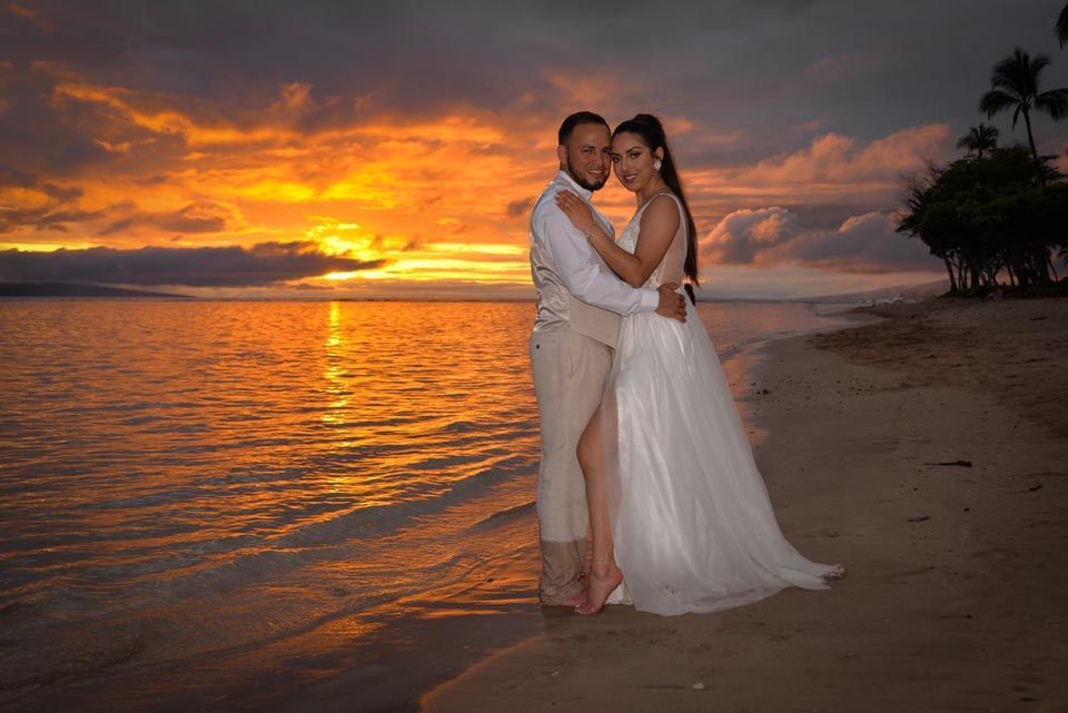couple standing in water on beach at sunset