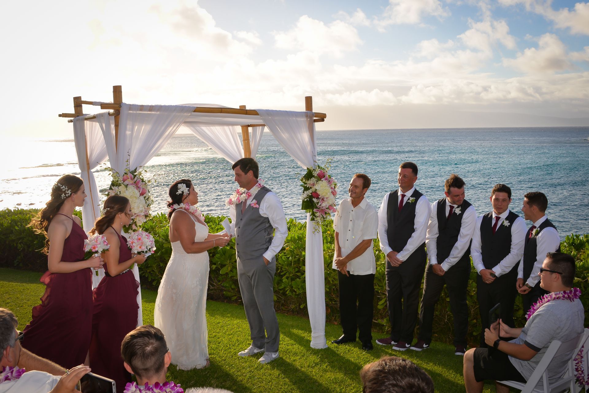 Wedding ceremony near the ocean with a bride and groom, bridesmaids, and groomsmen.