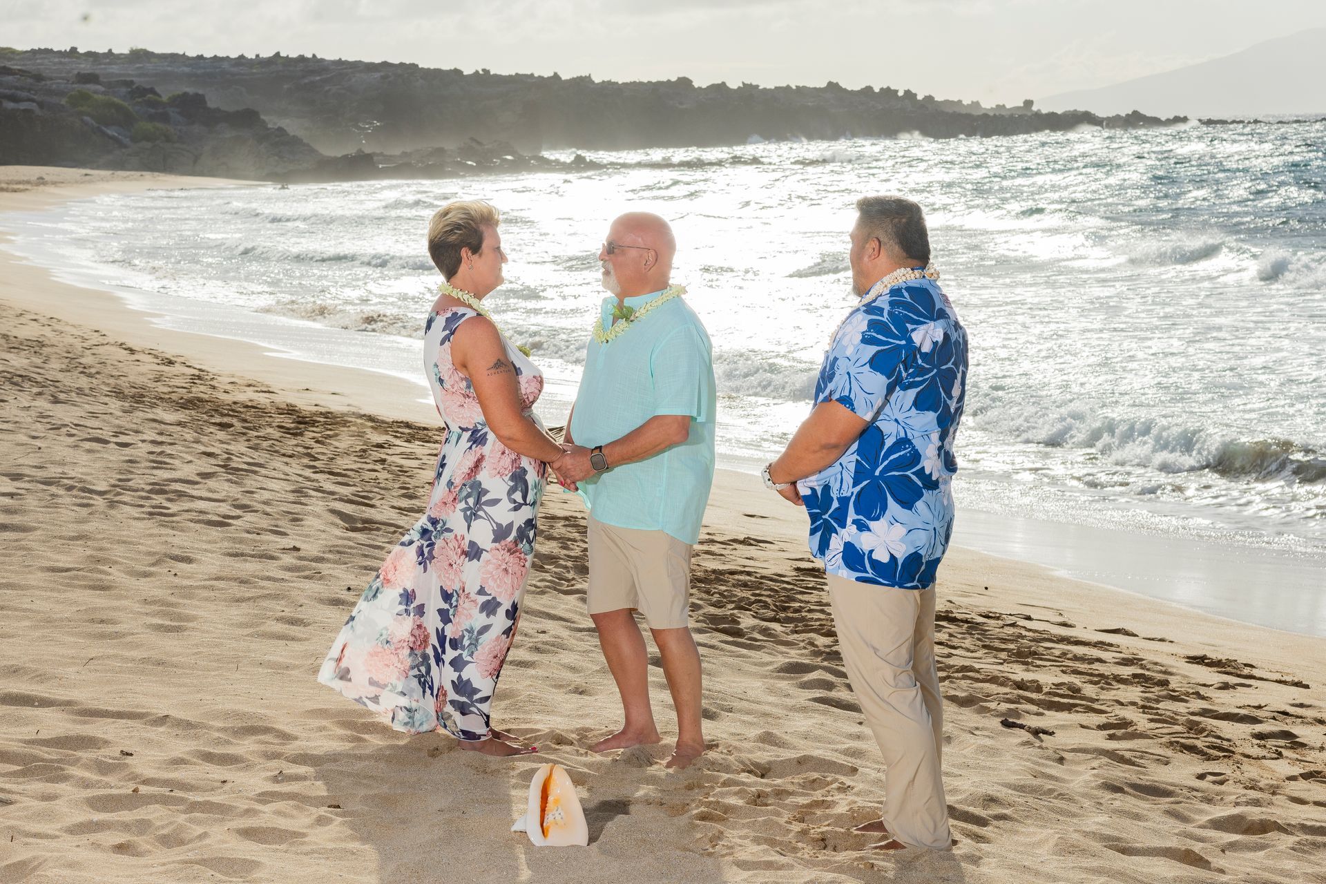 Couple getting married on a beach, officiant at right. Ocean waves in background.