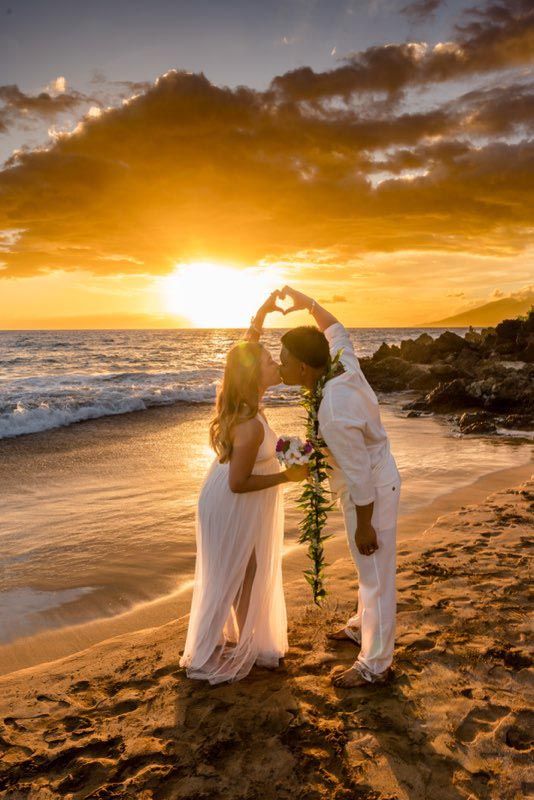 couple making hand heart on beach during sunset