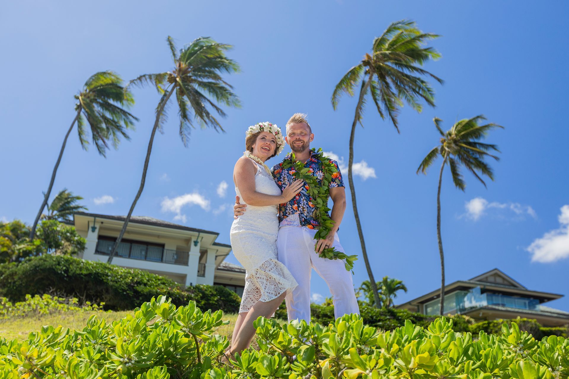 Couple embraces on a tropical beach, palm trees swaying, sunny blue sky.