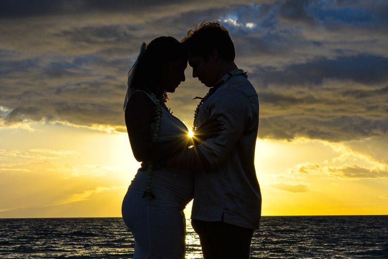 Silhouette of a couple embracing at sunset on a beach, with sunlight glowing between them.