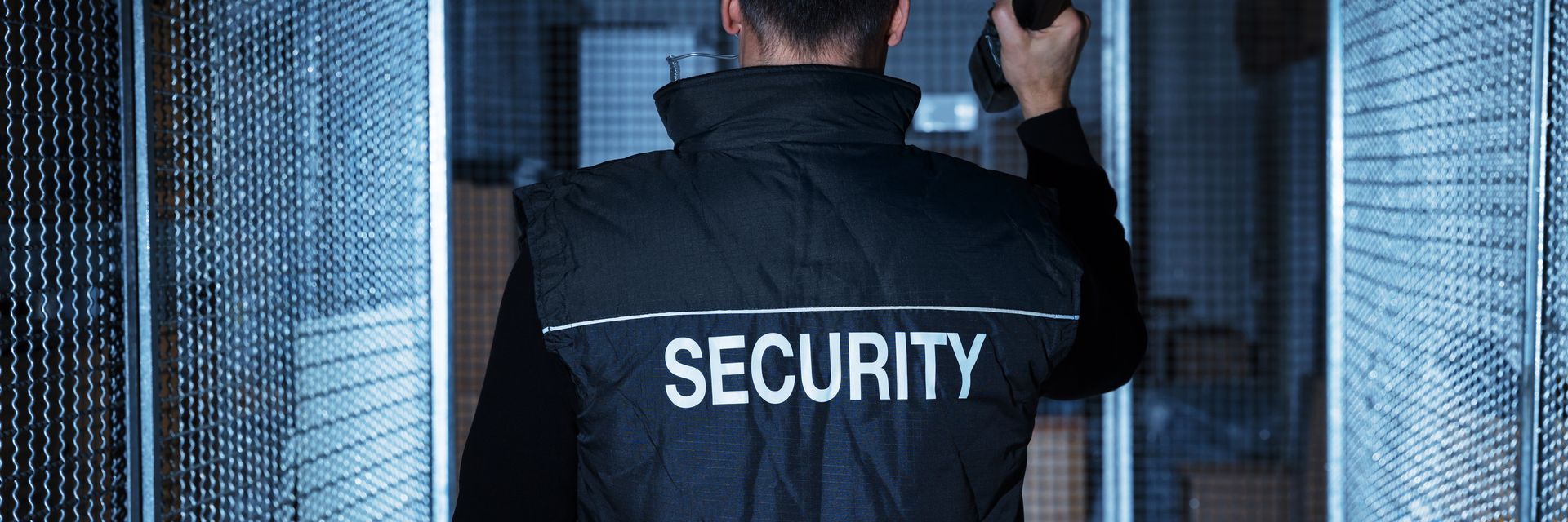 Security guard in black vest with “SECURITY” walking through a doorway.