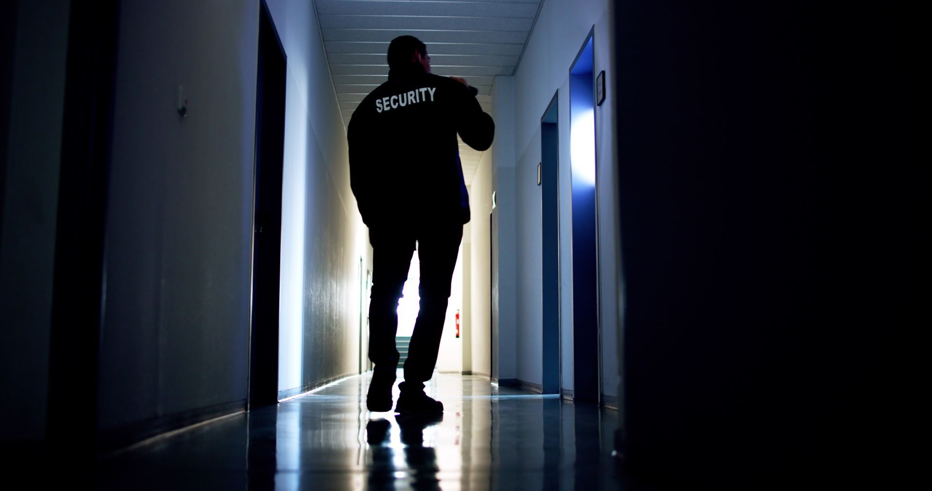 Security guard walking down a dim hallway, back to the camera.