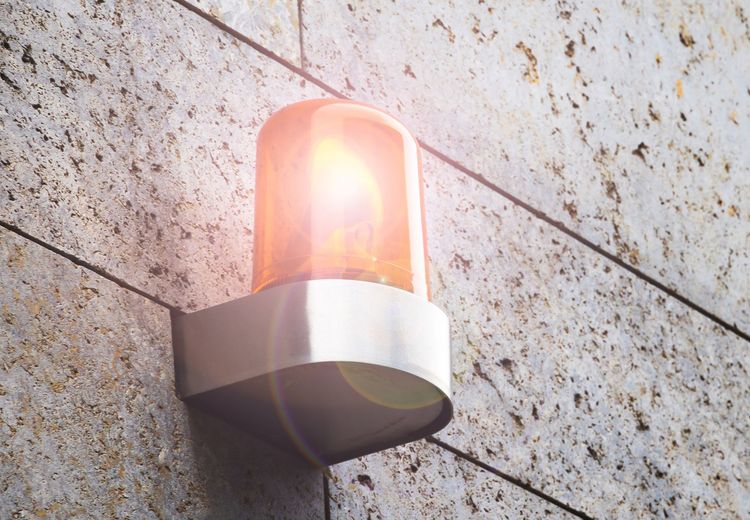Orange flashing emergency light mounted on a textured, white stone wall.