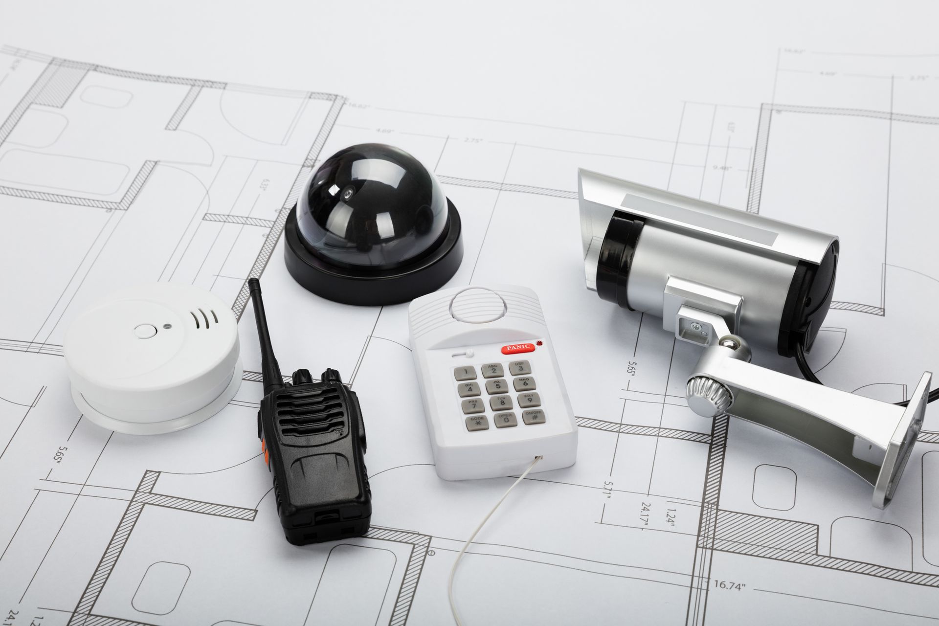 Security system components on a blueprint: camera, dome camera, keypad, walkie-talkie, and smoke detector.