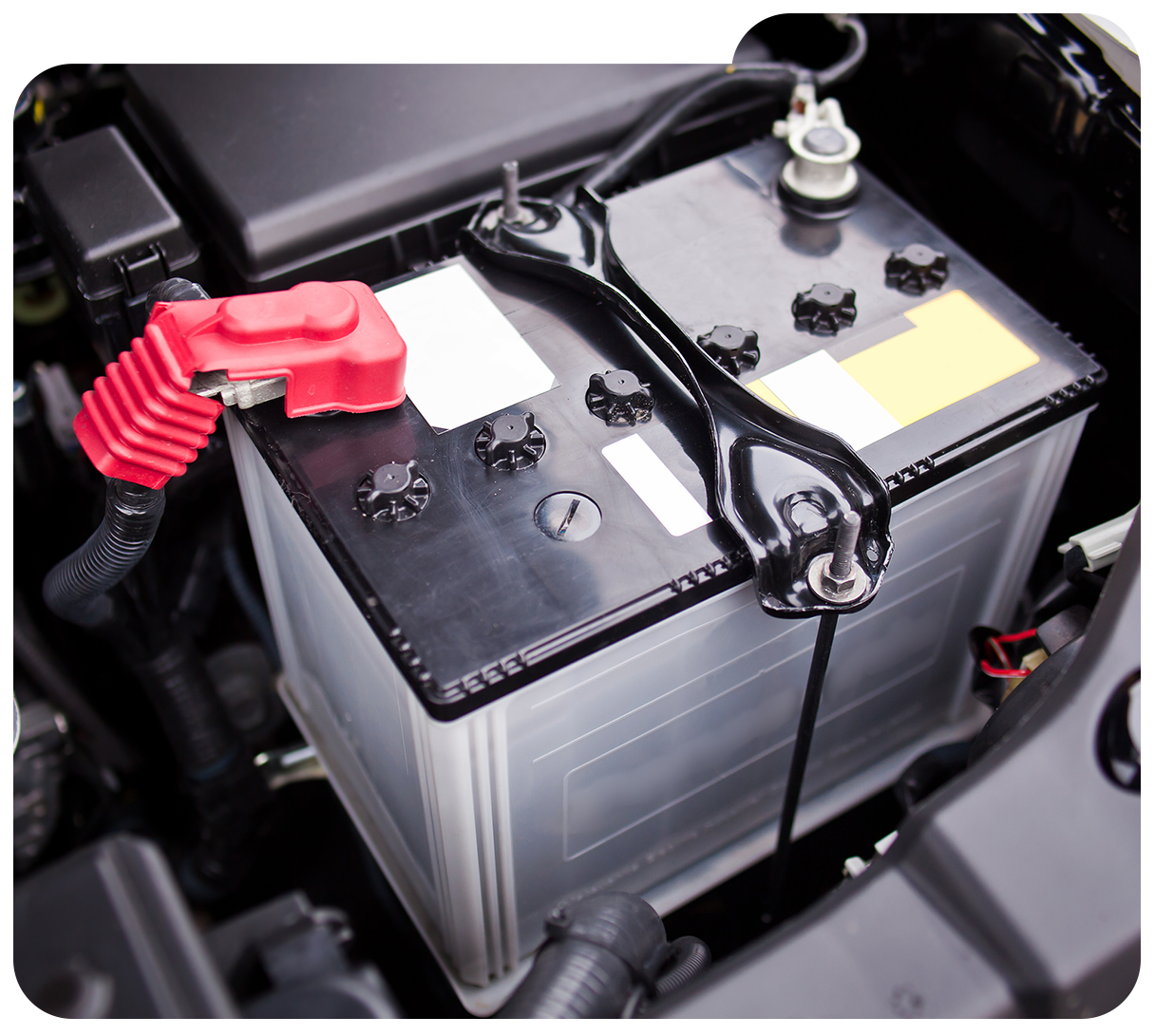 Car battery in a vehicle engine bay with red and black terminals attachedChecked checkbox icon with a bold black checkmark in a rounded square box
