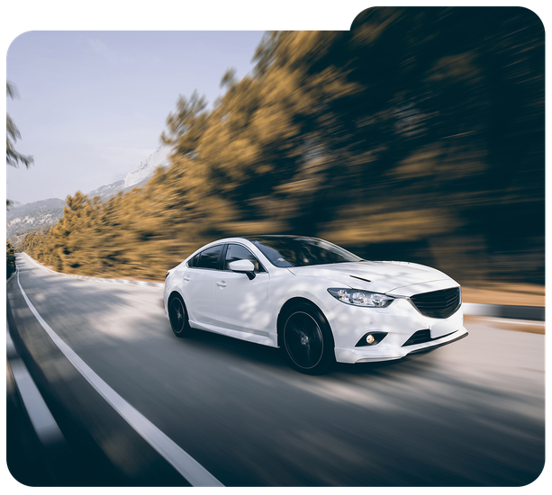 White sedan speeding on a curving road with motion blur and trees in the background