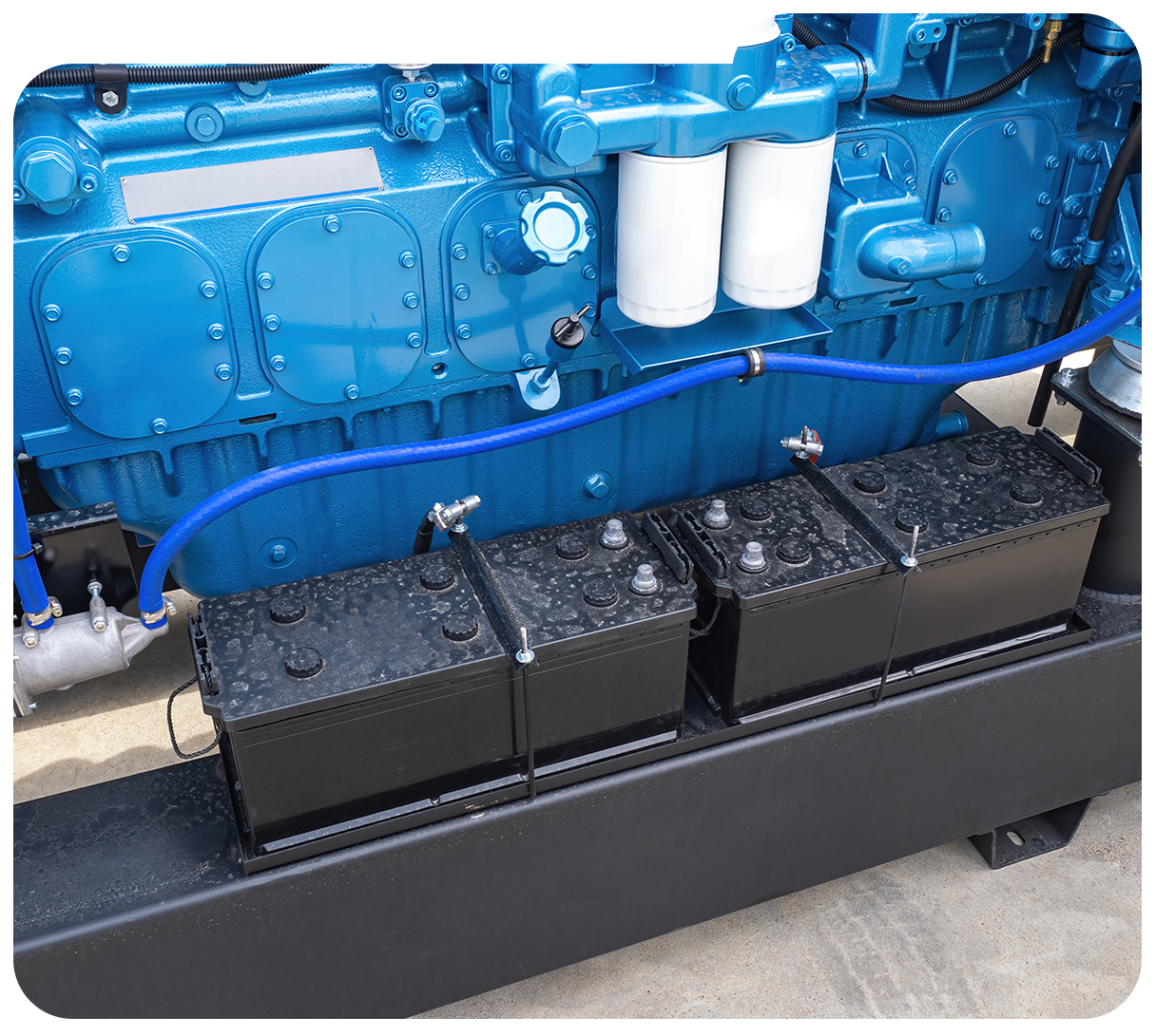 Blue engine with black batteries mounted in a compartment, with white filters and hoses visible.