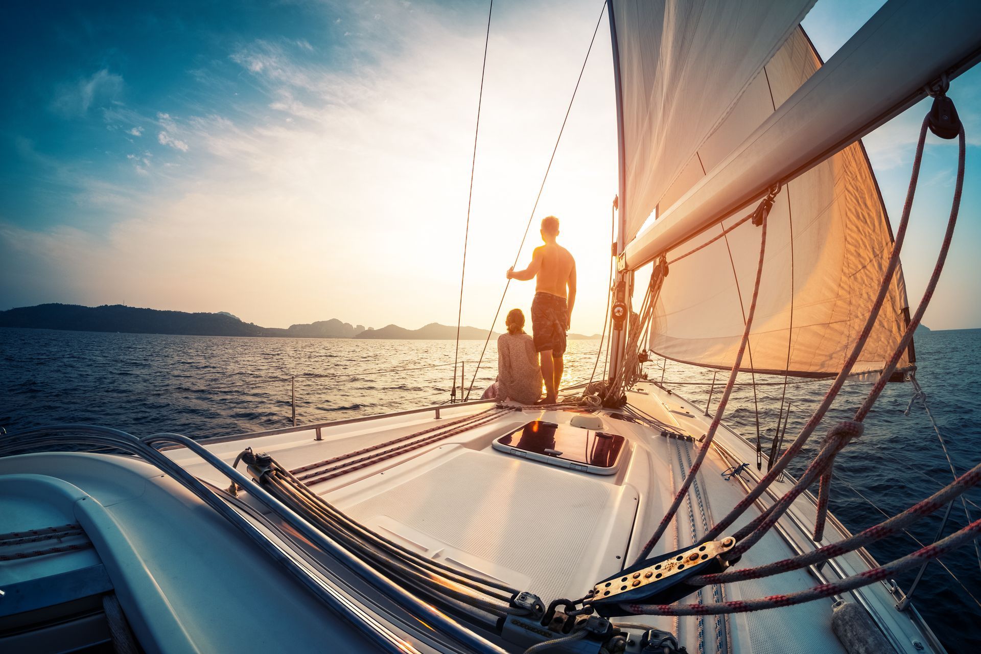 Sunlit sailboat deck with two people sailing on calm water at sunset