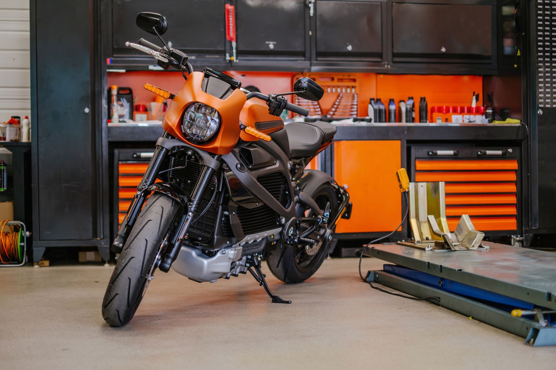 Orange motorcycle parked in a garage workshop with tools and cabinets in the background
