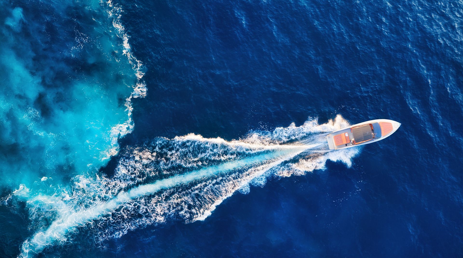 Speedboat cutting through deep blue water, leaving a white wake and turquoise spray.