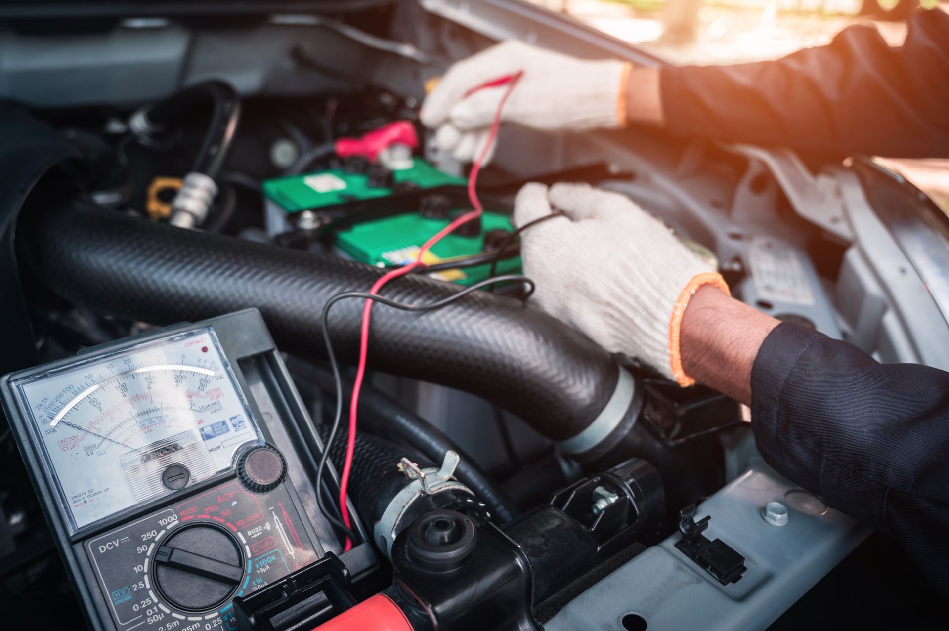 Mechanic testing a car battery with a multimeter under the hood, with red and black wires connected