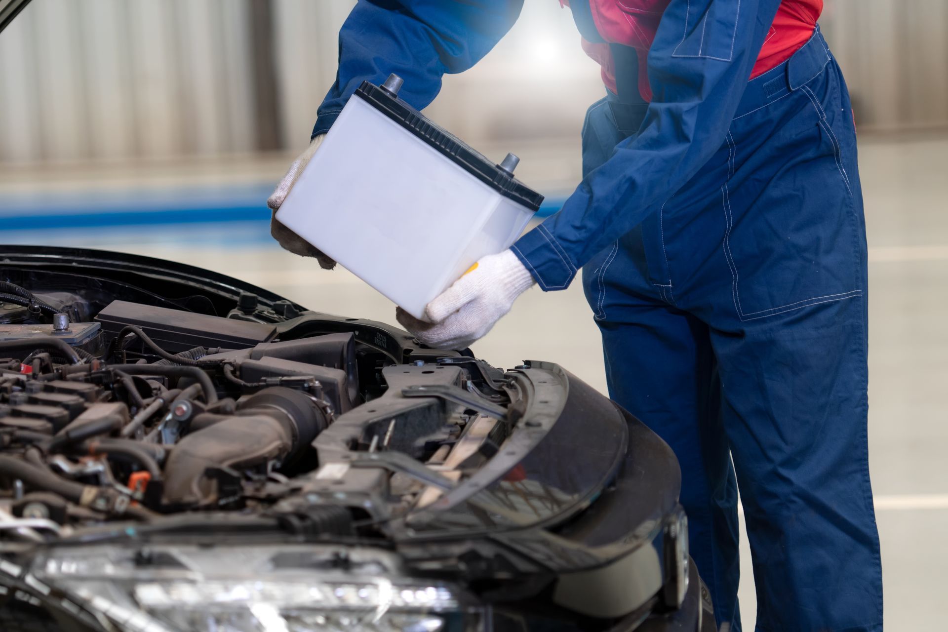 Mechanic in blue coveralls checking car engine with a clipboard in a garage