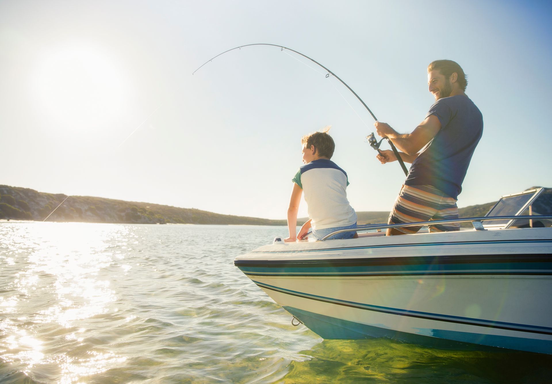 Two people fishing from a boat on a sunny lake, with one rod arcing over the water.