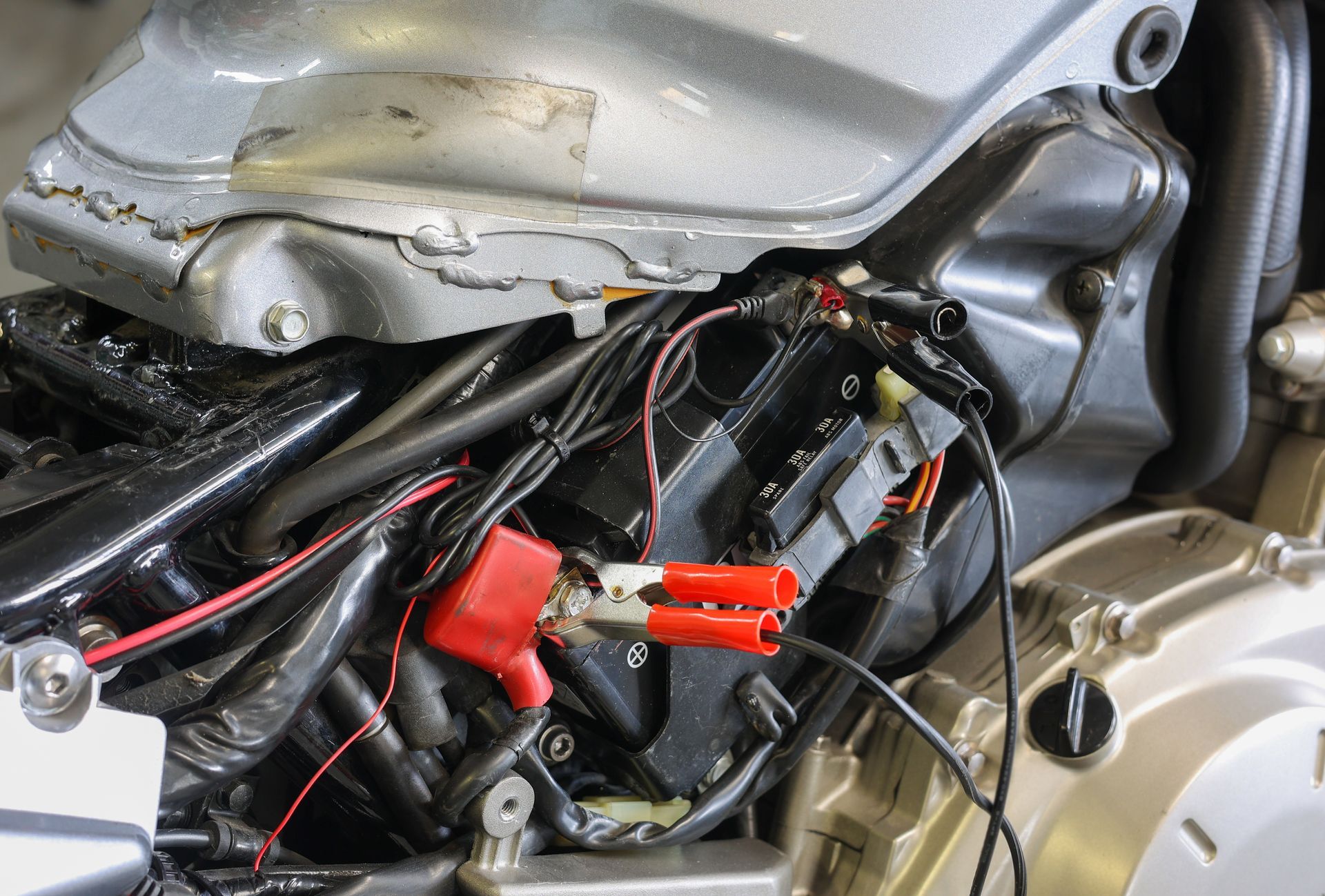 Close-up of a motorcycle engine with exposed wiring and a red connector under the fuel tank