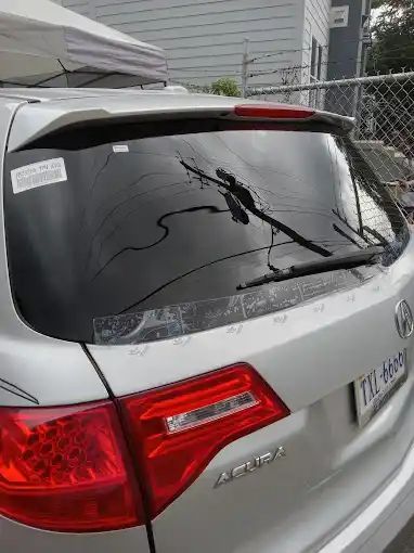A silver acura integra with a broken windshield is parked in front of a fence.