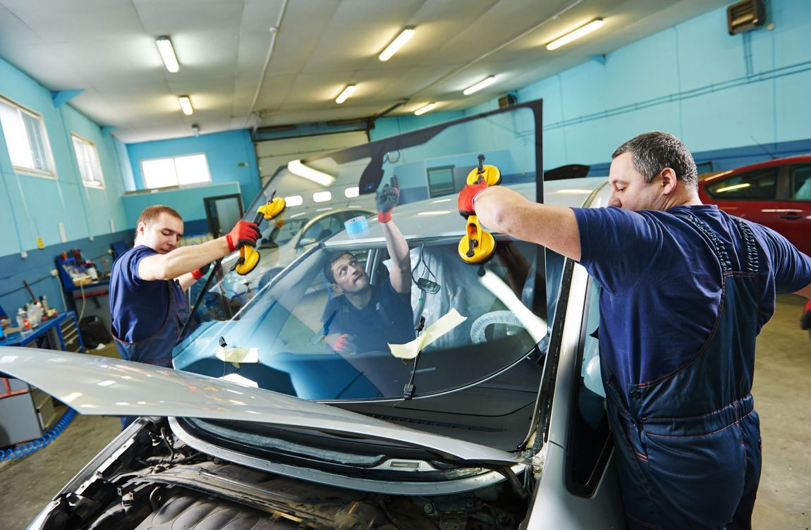 Workers replacing a car windshield in an auto repair shop