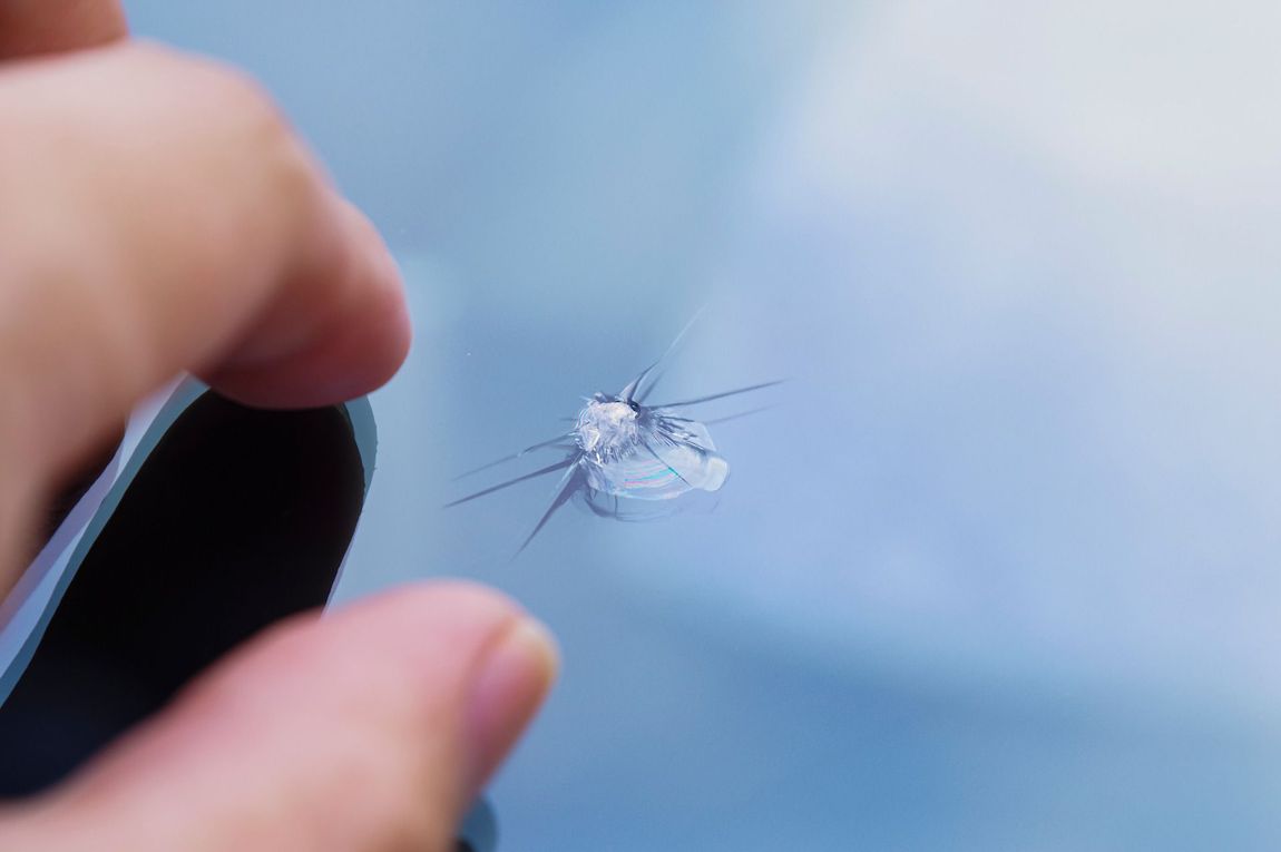 Cracked screen with a spiderweb fracture, held between a thumb and finger