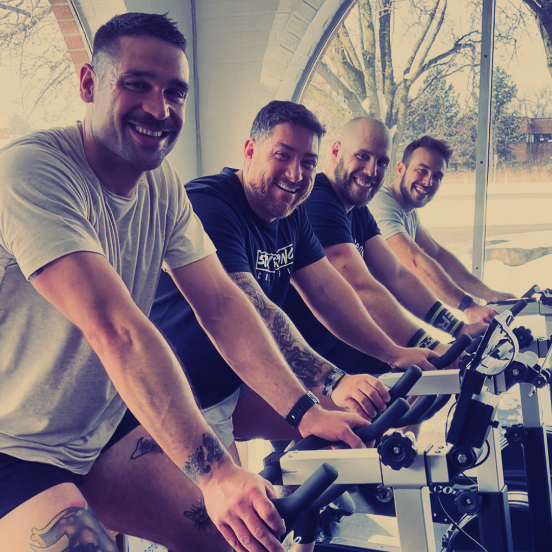 A group of men are riding exercise bikes in a gym.