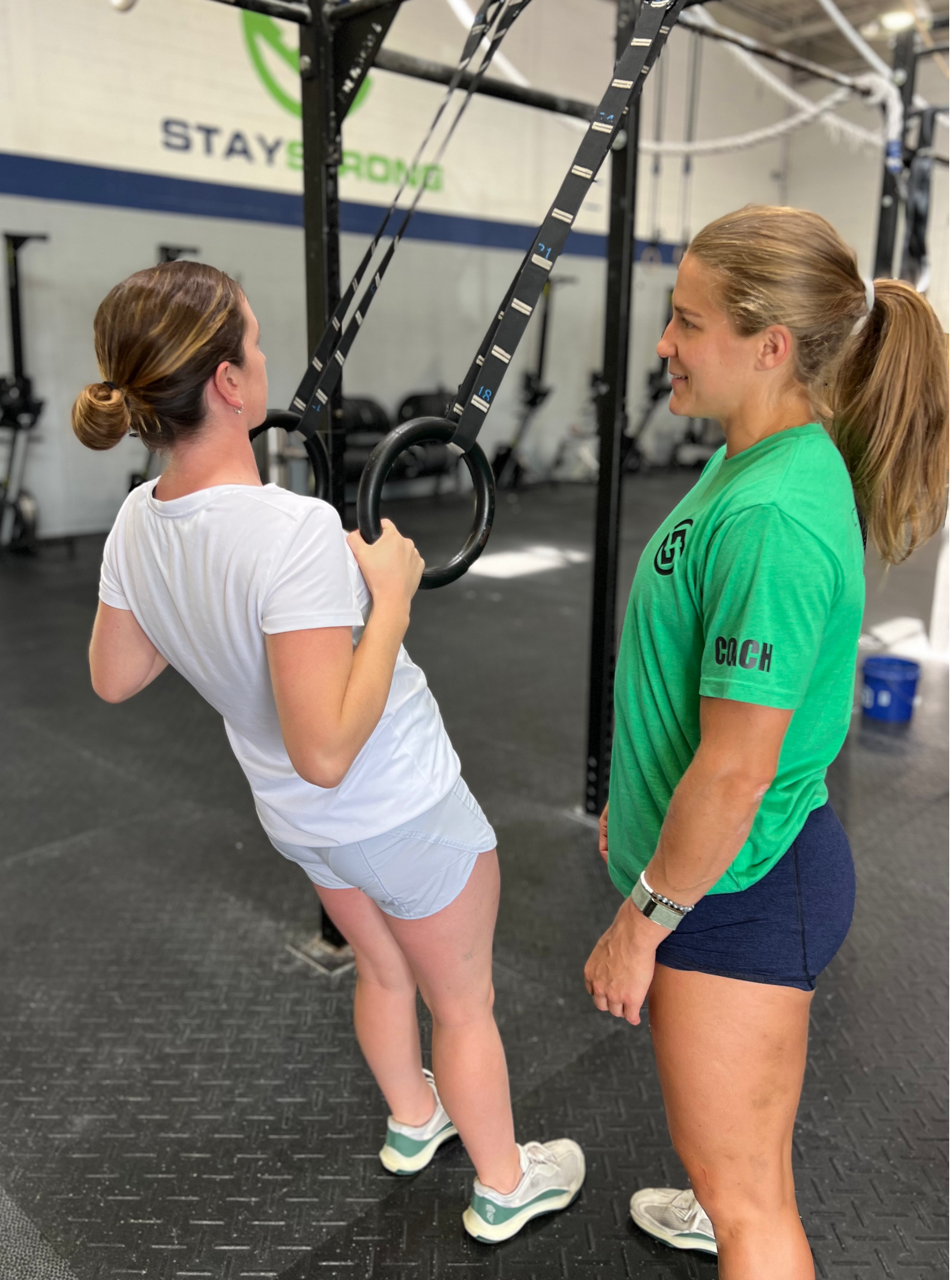 A woman in a green shirt is standing next to another woman in a gym.